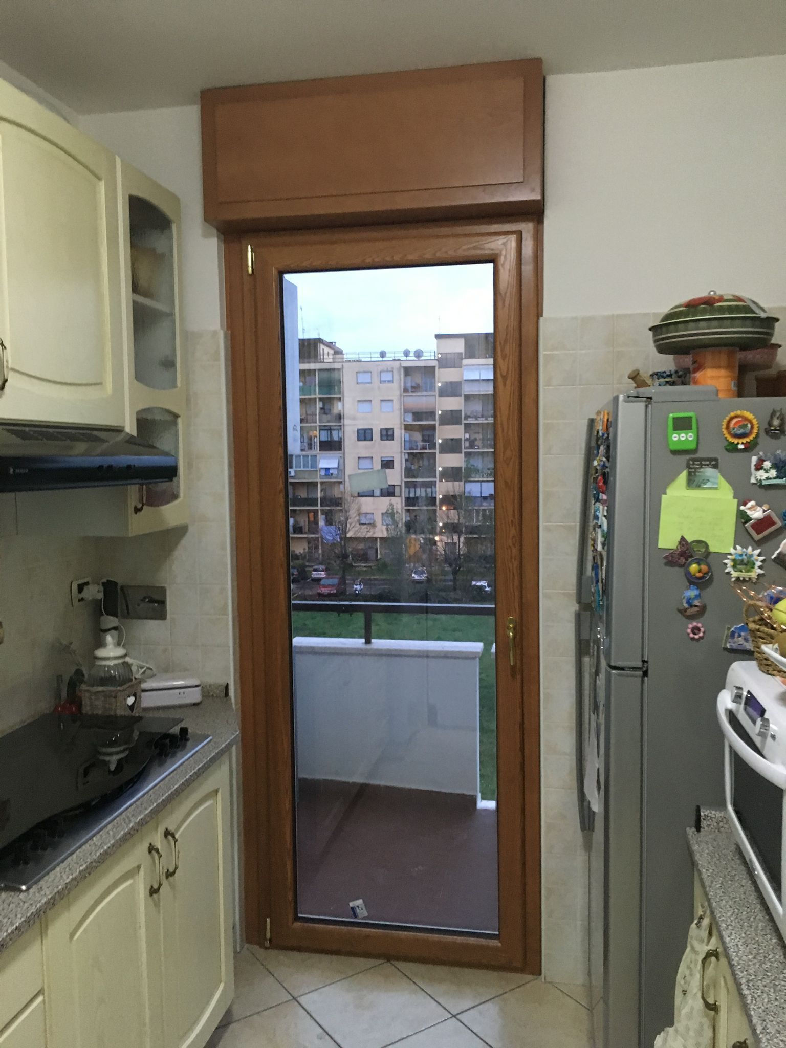 Cucina stretta con porta a vetri che si apre su un piccolo balcone e sui palazzi circostanti.