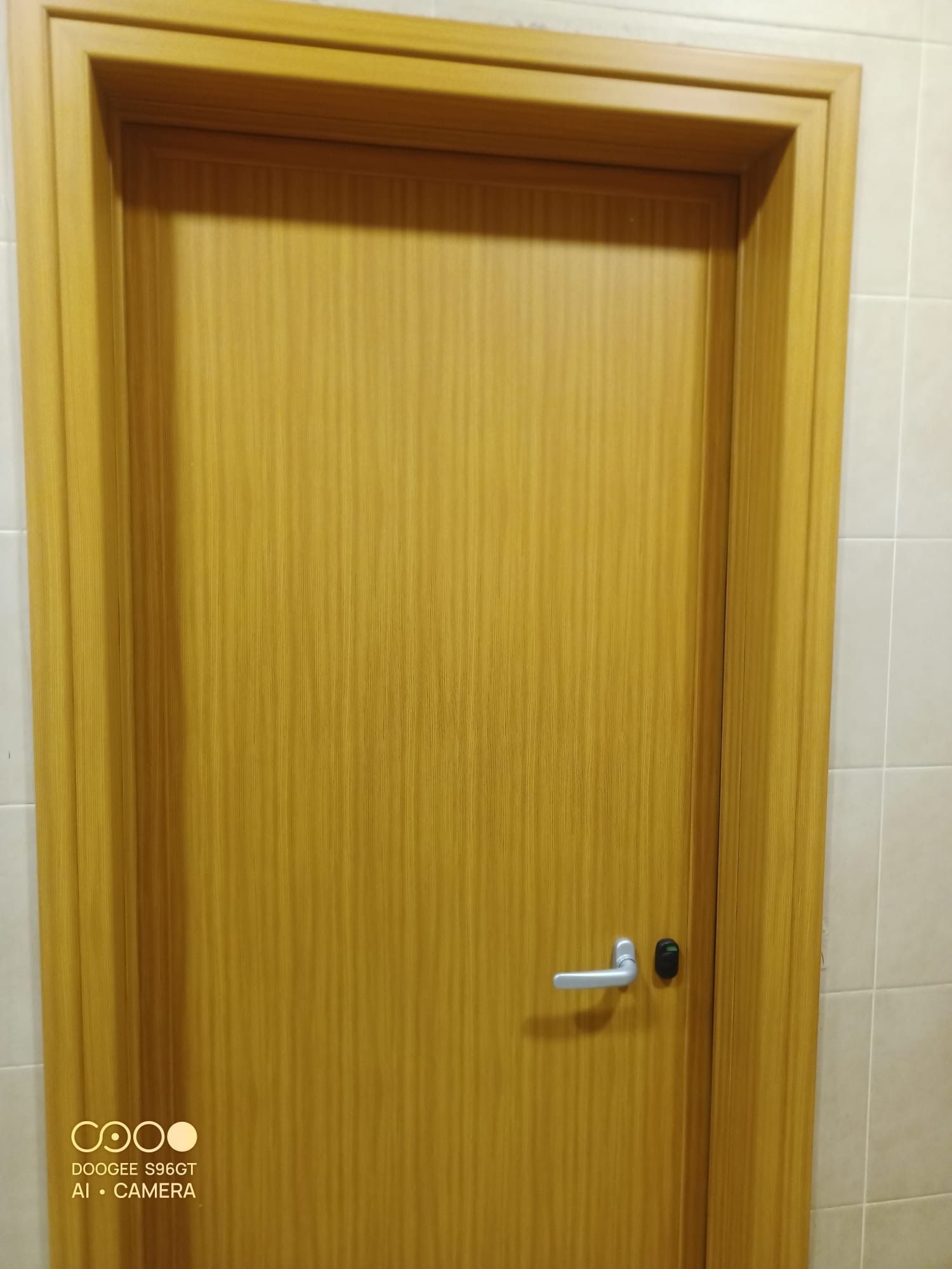 Porta di legno con maniglia argentata in un corridoio piastrellato di beige.