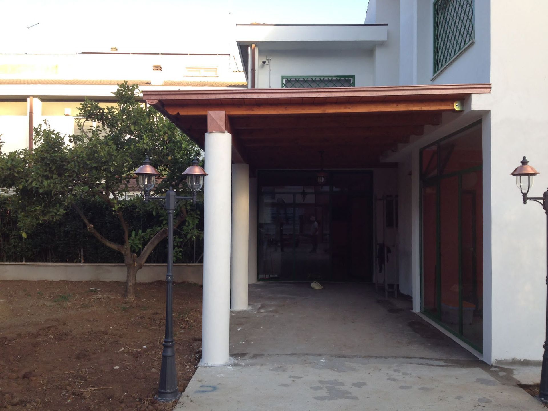 Passaggio coperto che conduce all'ingresso di un edificio con colonne bianche e tetto in legno.