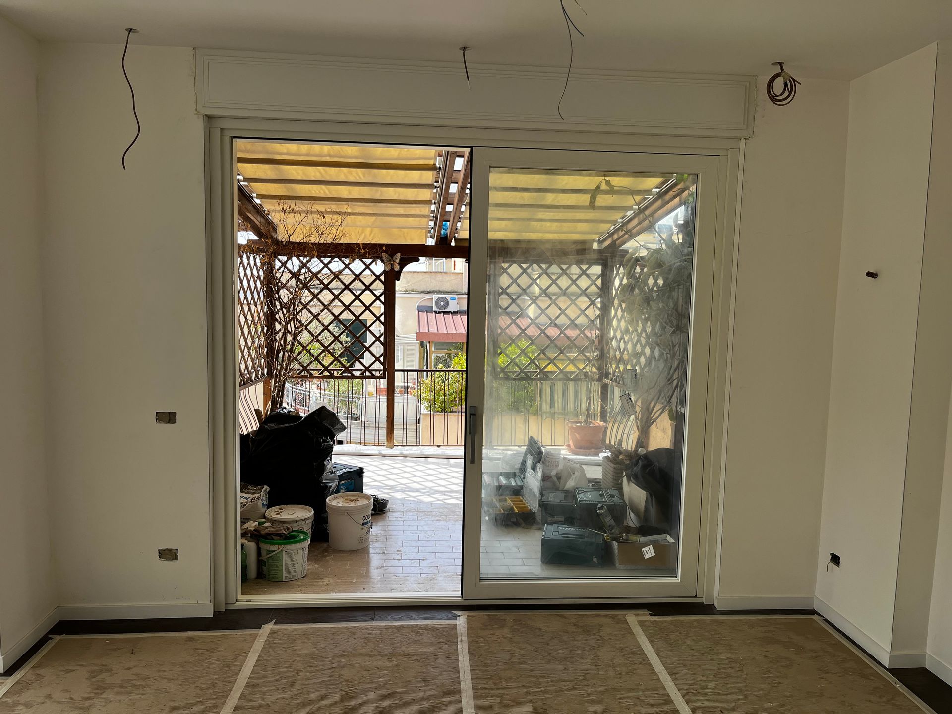 Stanza vuota con porte scorrevoli in vetro che si aprono su un patio e un pergolato da giardino.