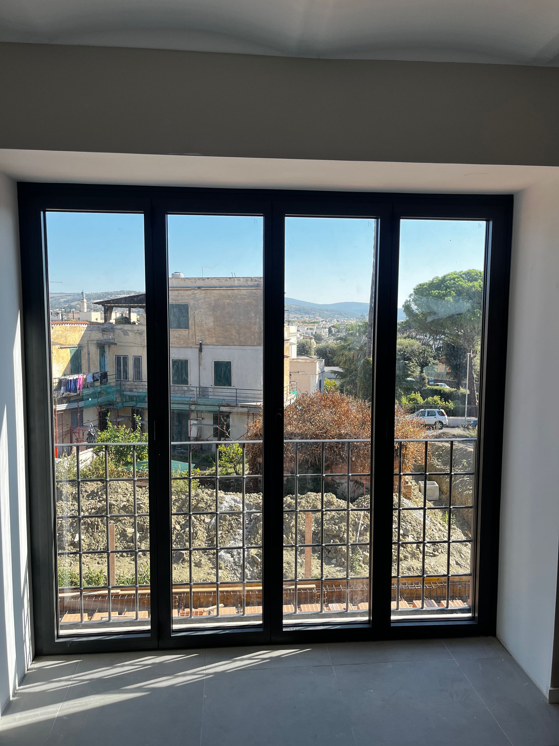 Vista attraverso una finestra con le sbarre su un quartiere soleggiato e sulle colline in lontananza.