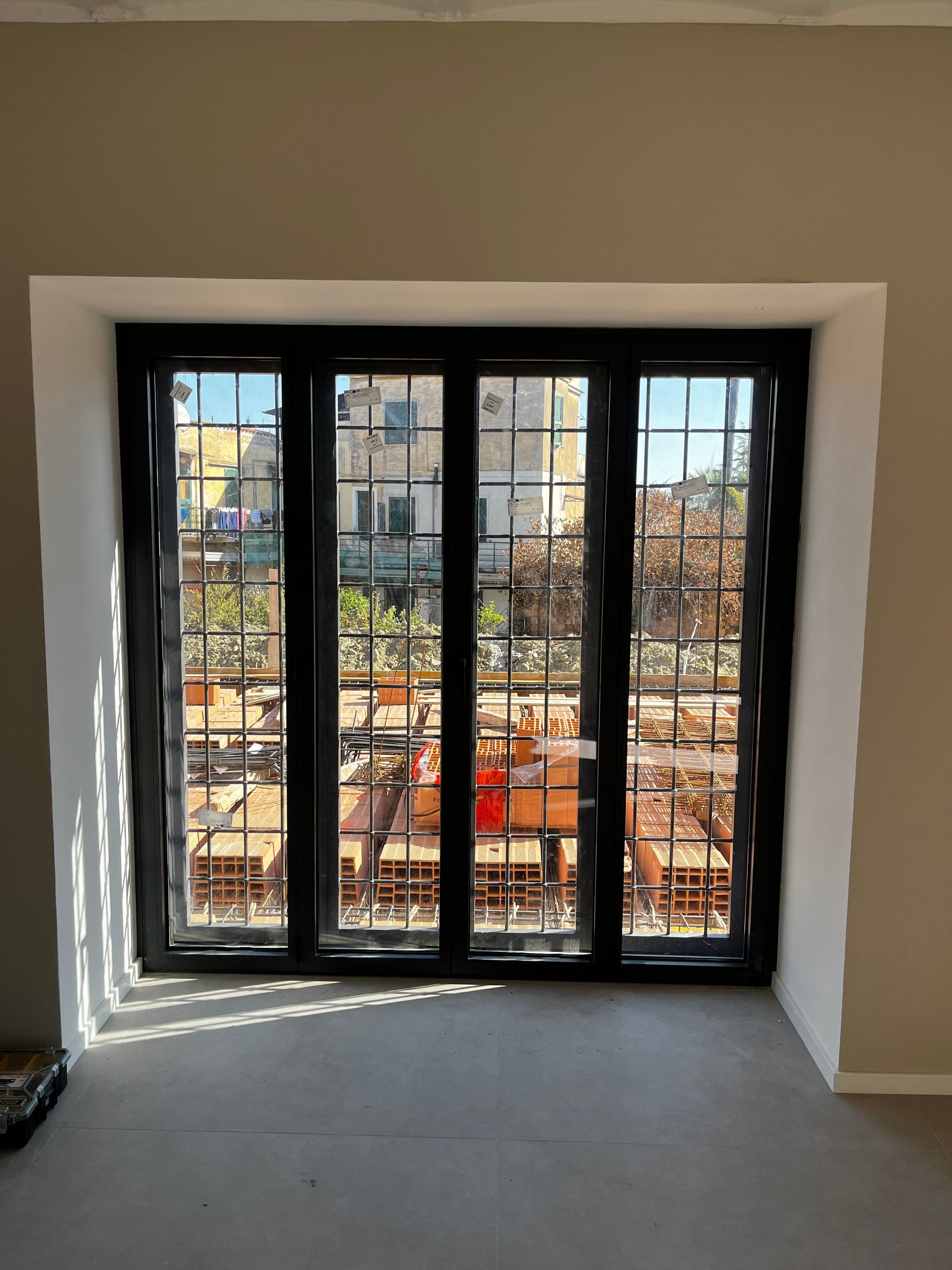 Stanza vuota con grande finestra con cornice nera che si affaccia su un cantiere.