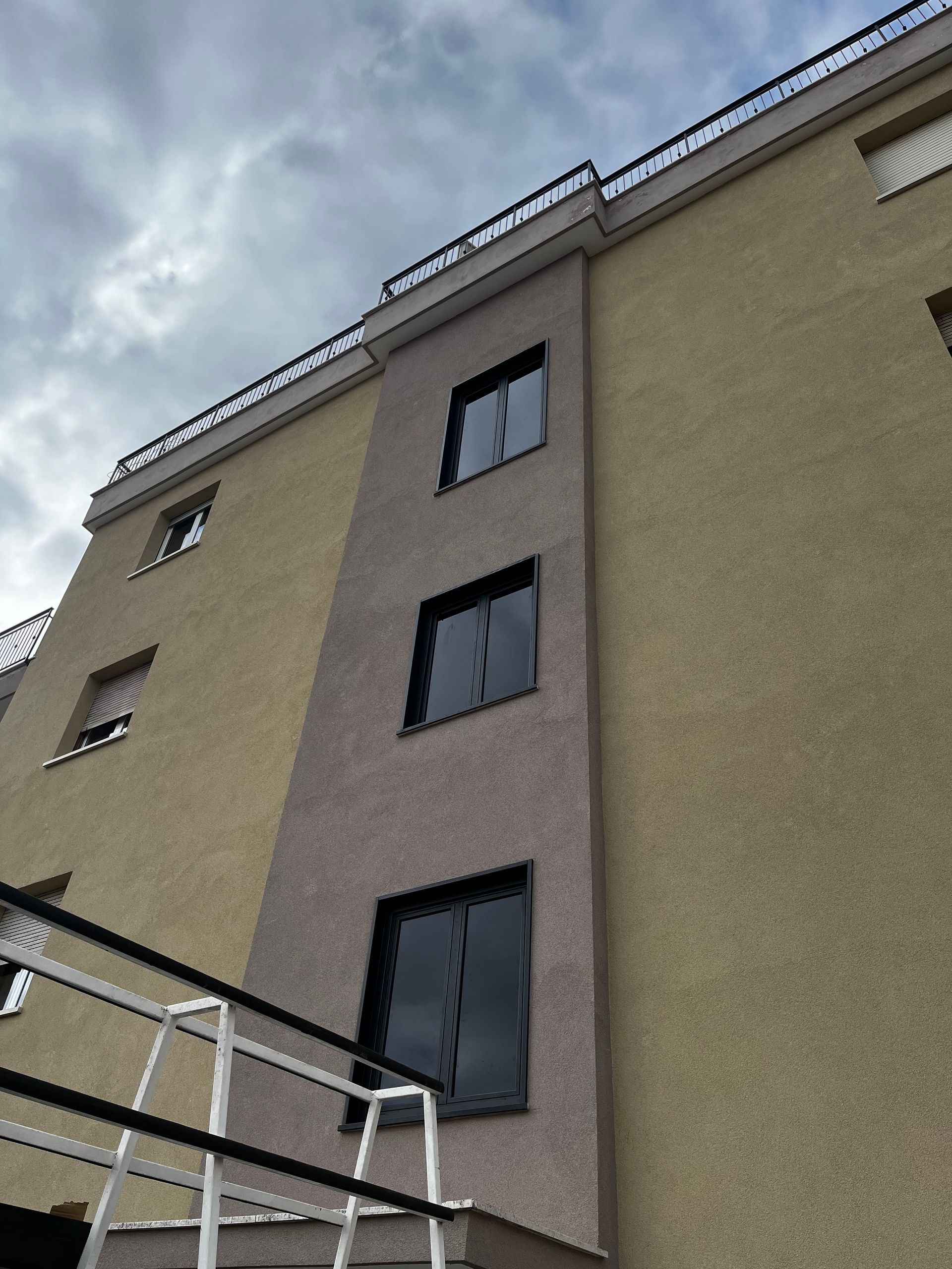 Vista dal basso di un condominio beige con finestre scure e un cielo nuvoloso sopra.