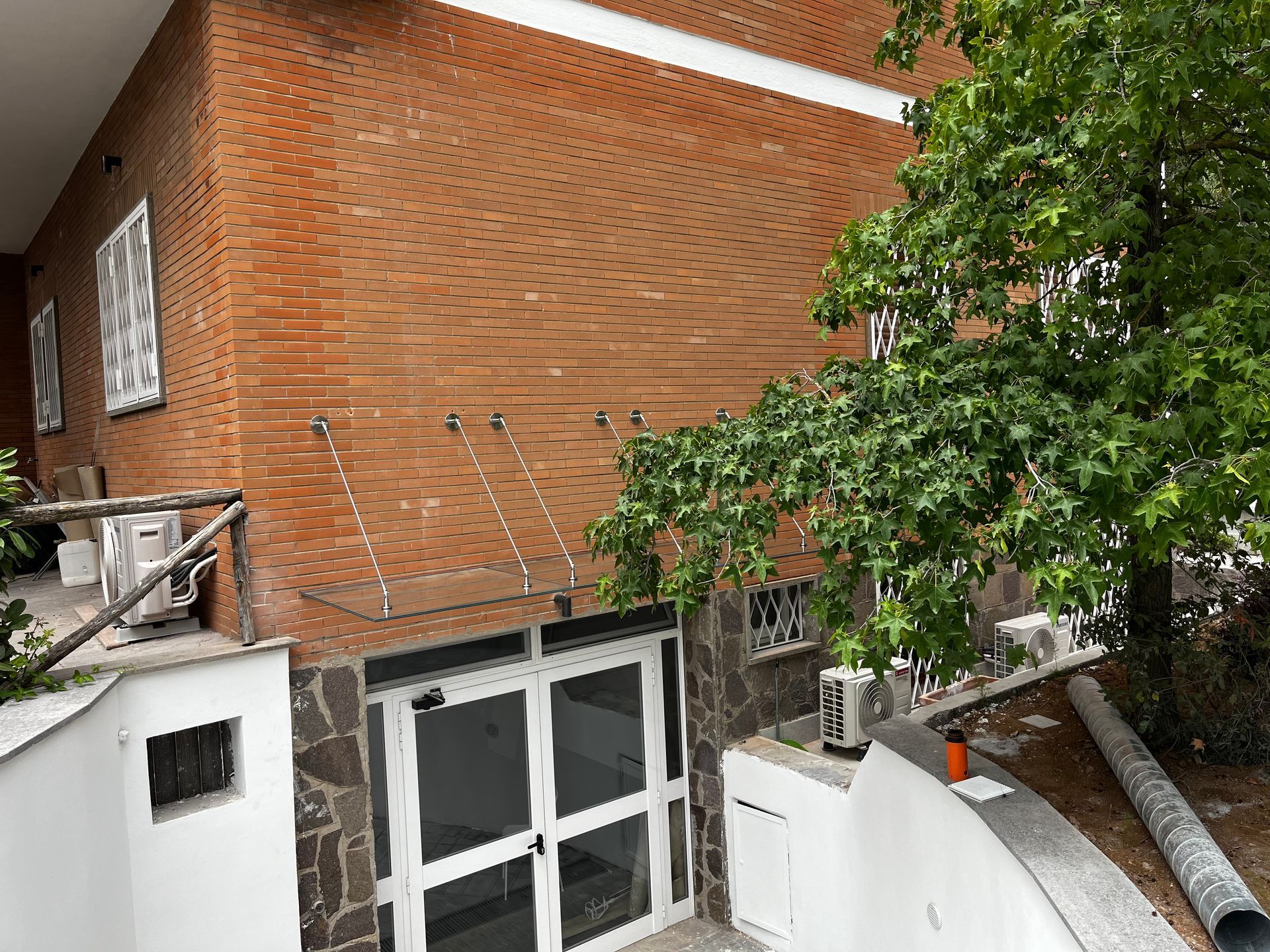 Edificio in mattoni con finestre incorniciate di bianco e un albero frondoso in primo piano.