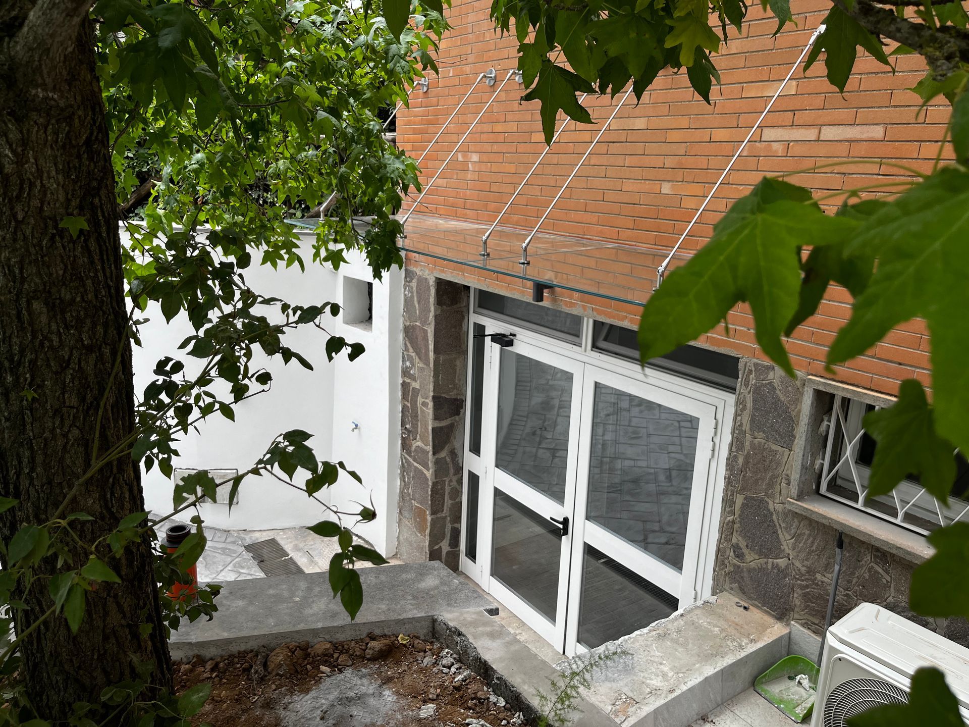 Esterno della casa con porte e finestre bianche sotto un tetto di tegole rosse, visto attraverso i rami degli alberi.