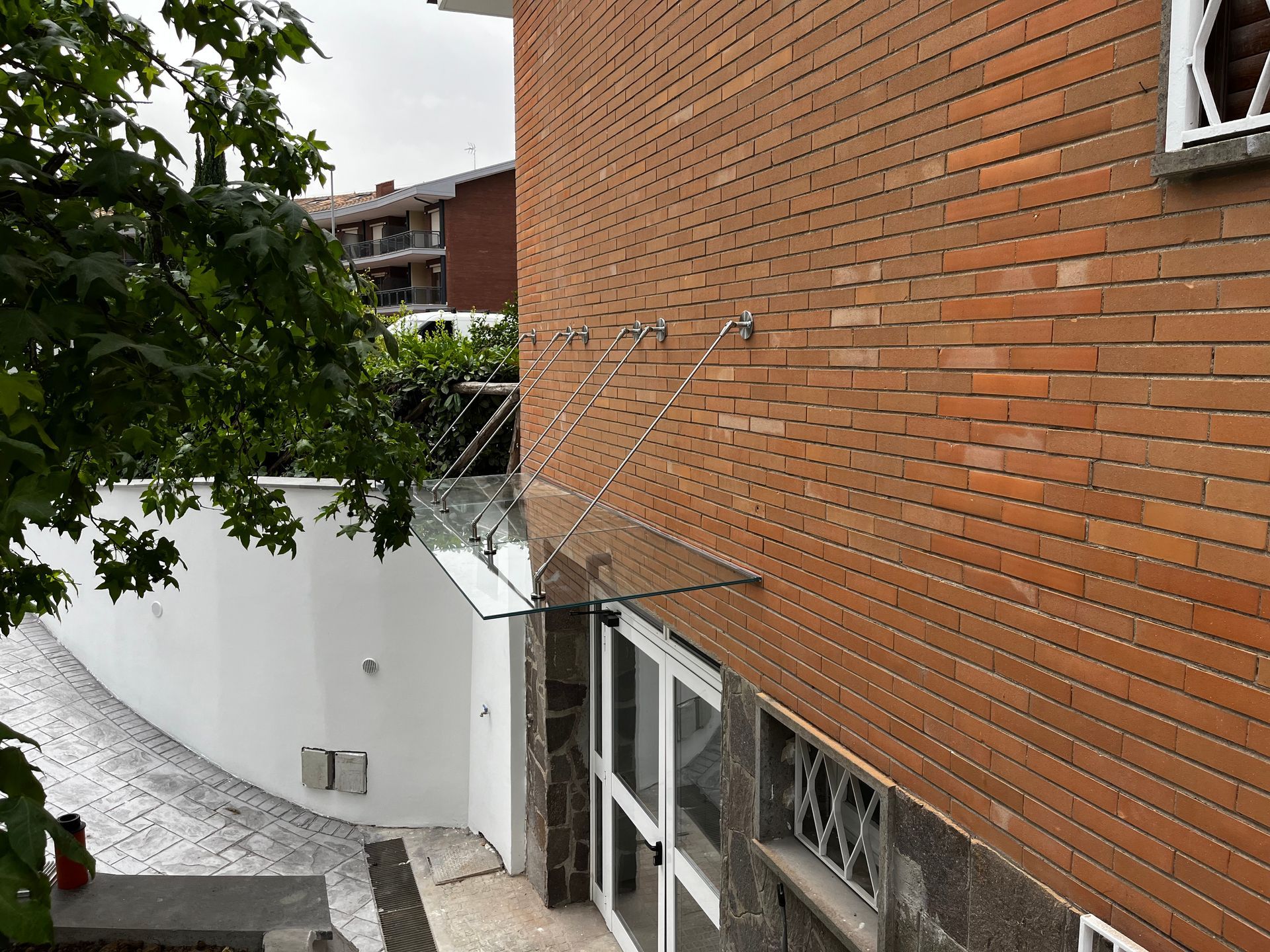 Palazzo di appartamenti in mattoni adiacente a uno stretto cortile con muri bianchi e una tettoia in vetro.