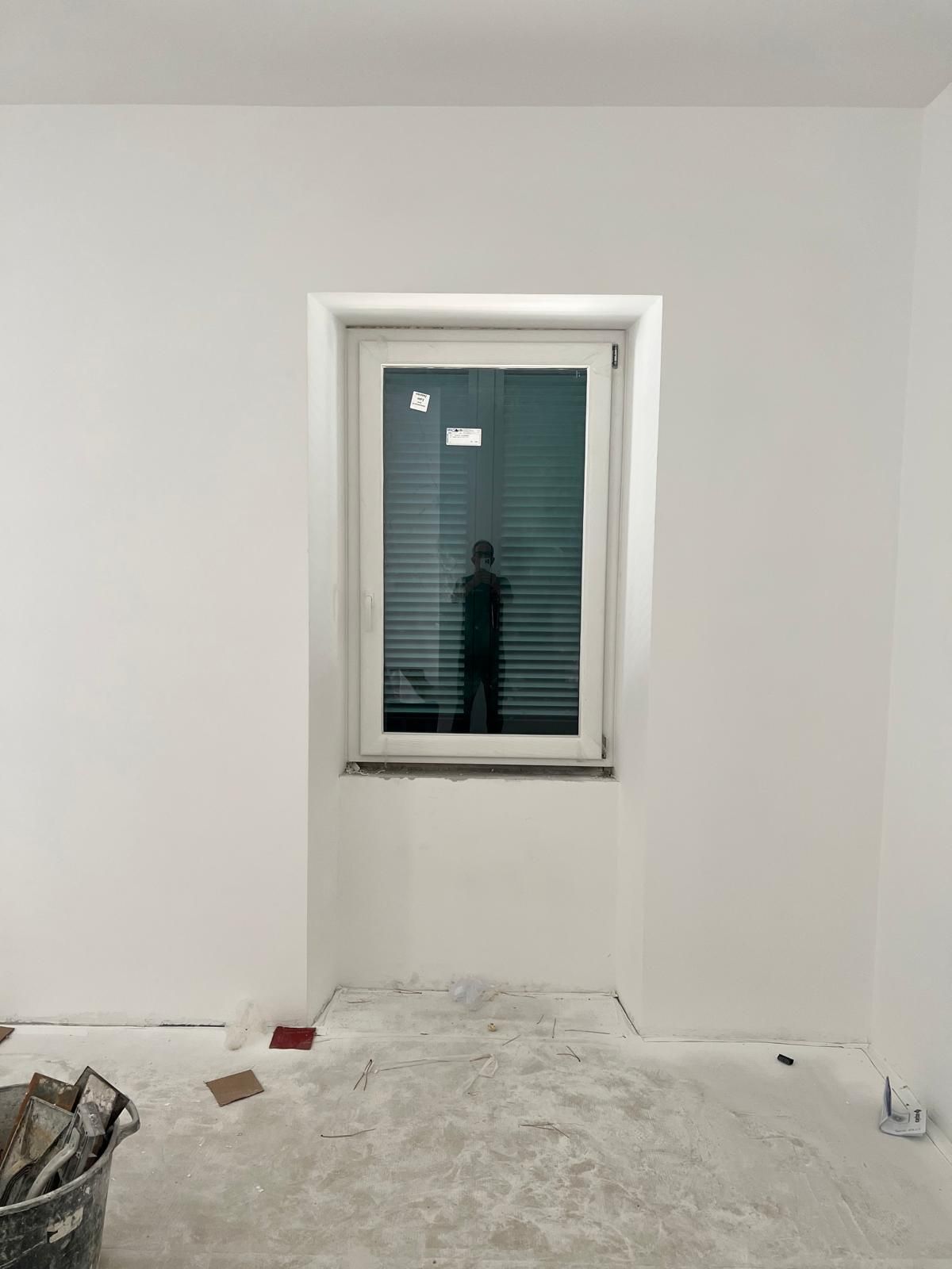 Piccola stanza bianca con pavimento non rifinito e un'unica finestra sulla parete di fondo.