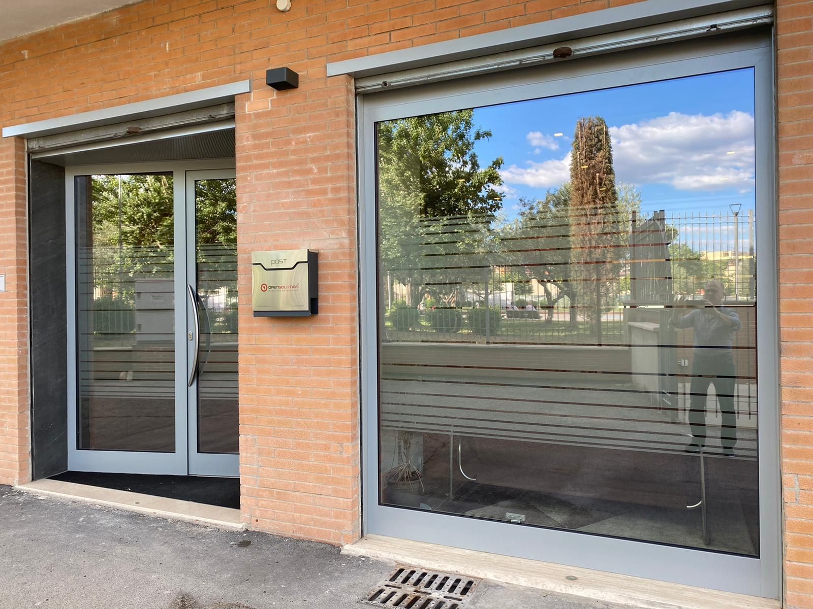 Vetrina in mattoni con porte a vetri e un'ampia finestra riflettente che mostra gli alberi all'esterno