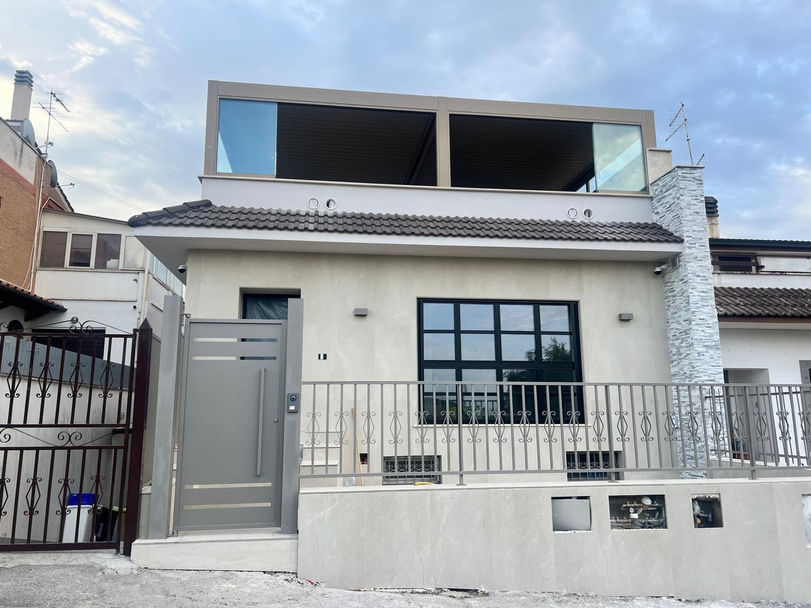 Casa moderna a due piani con cancello grigio, facciata bianca e ampie finestre al piano superiore.