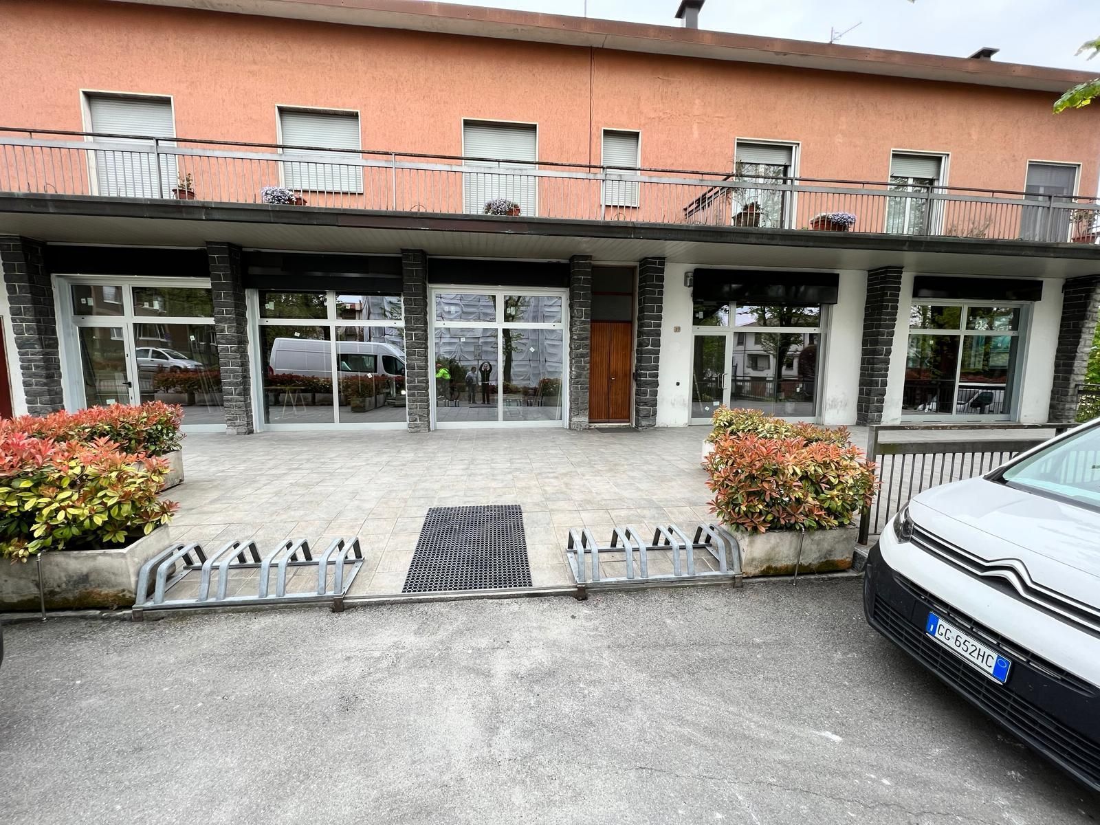 Ingresso dell'edificio con porte a vetri, ringhiere bianche, fioriere e un'auto parcheggiata sulla destra.
