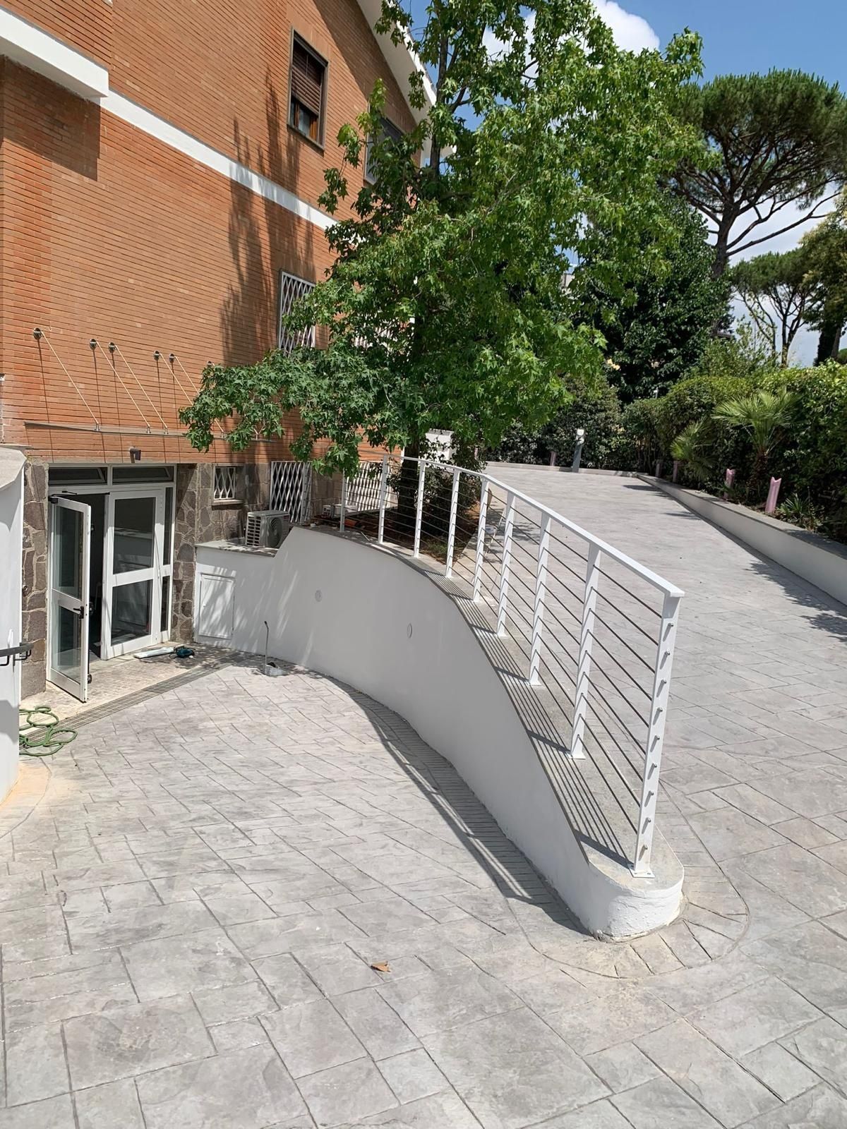 Edificio in mattoni accanto a una rampa inclinata in cemento con ringhiere bianche e alberi lungo il percorso.