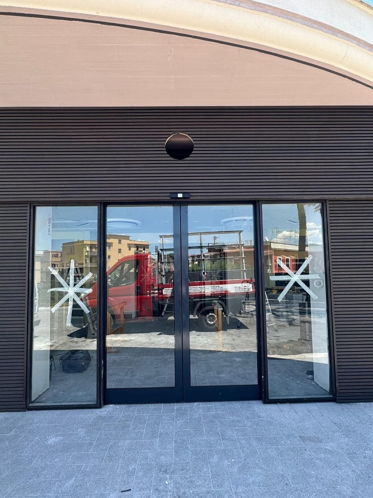 Facciata del negozio in vetro con porte scorrevoli nere e decorazioni a stella bianche, che riflettono i veicoli parcheggiati all'esterno.