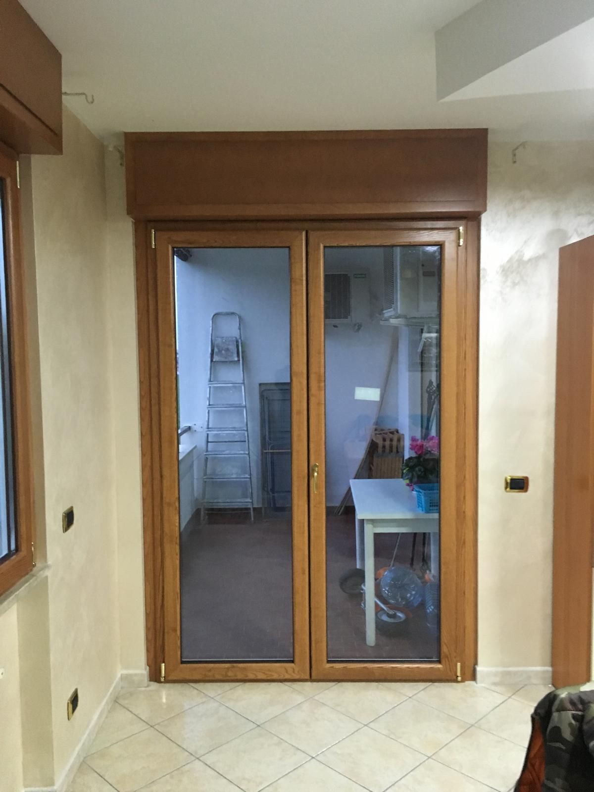 Porte scorrevoli in vetro con telaio in legno in un corridoio piastrellato, che mostrano una stanza con una scala e un tavolo all'interno