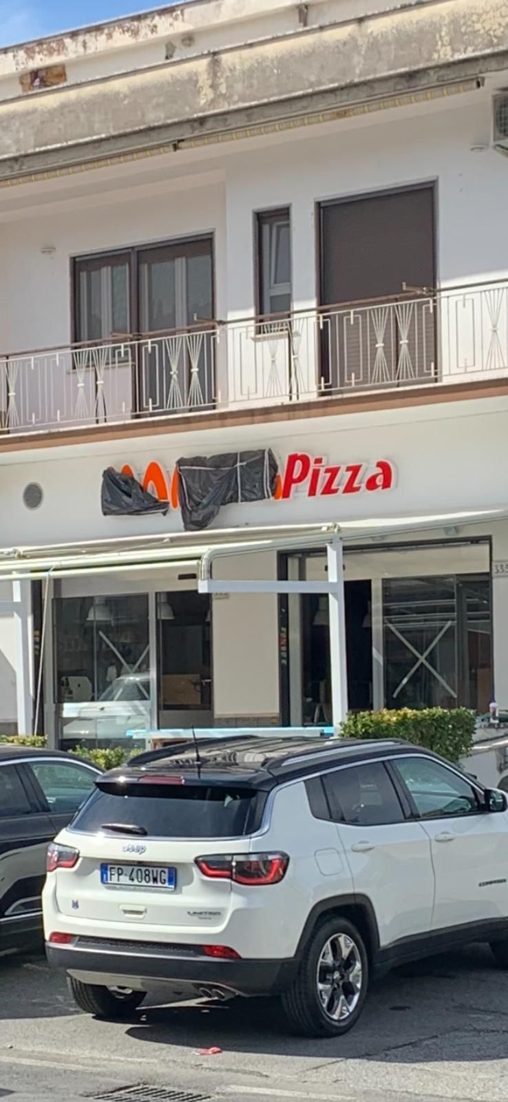 Vetrina di una pizzeria con un SUV bianco parcheggiato davanti