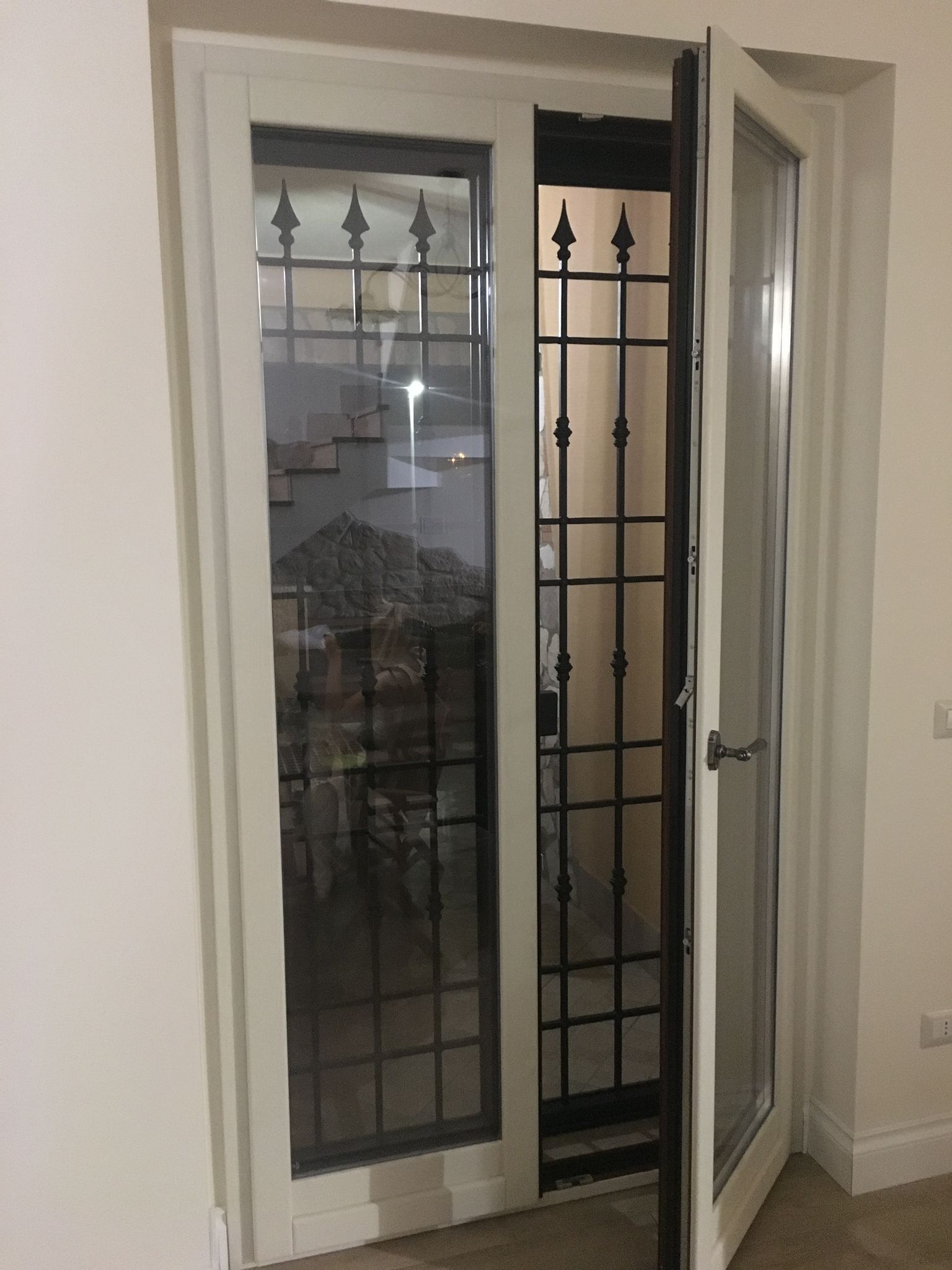 Porta a vetri con cornice bianca e cancello di sicurezza nero, leggermente aperta su un balcone o un patio.