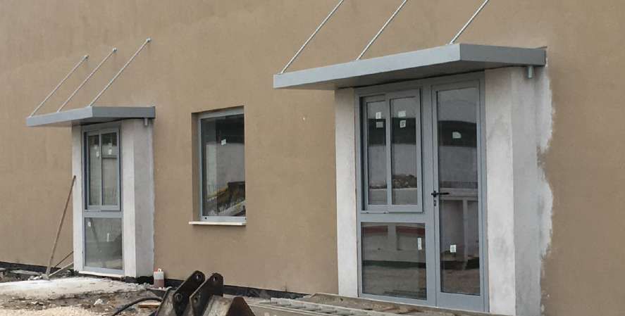 Esterno di un edificio beige con due porte grigie e tettoie metalliche sopra gli ingressi.