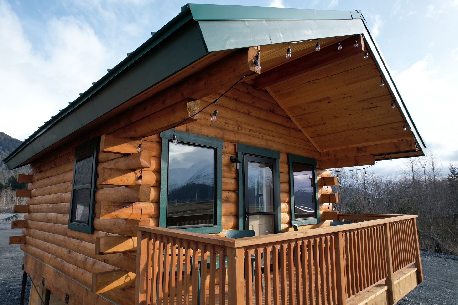 A small log cabin with a balcony and mountains in the background
