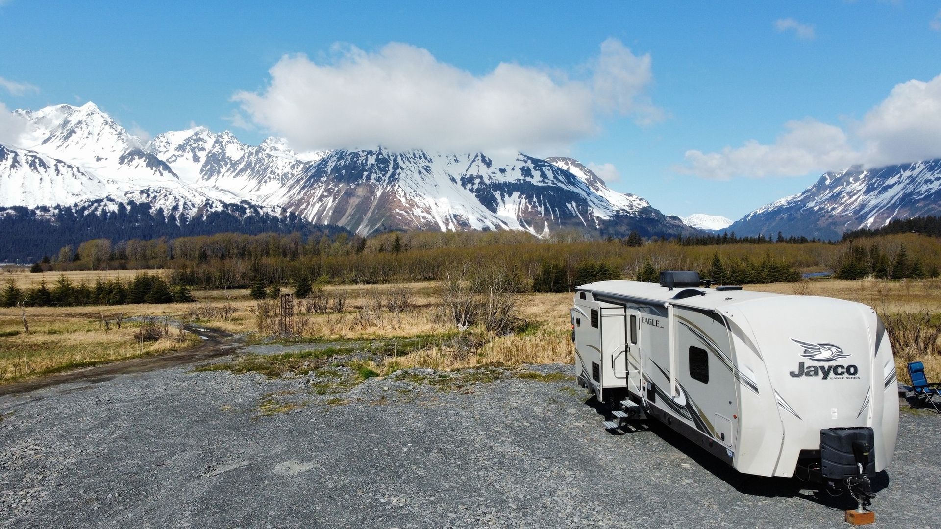 A jayco trailer is parked in a gravel lot with snowy mountains in the background.