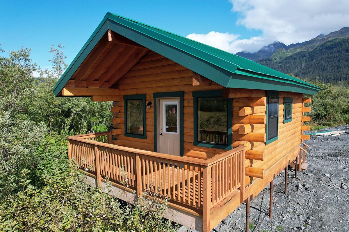 A small log cabin with a green roof and a deck