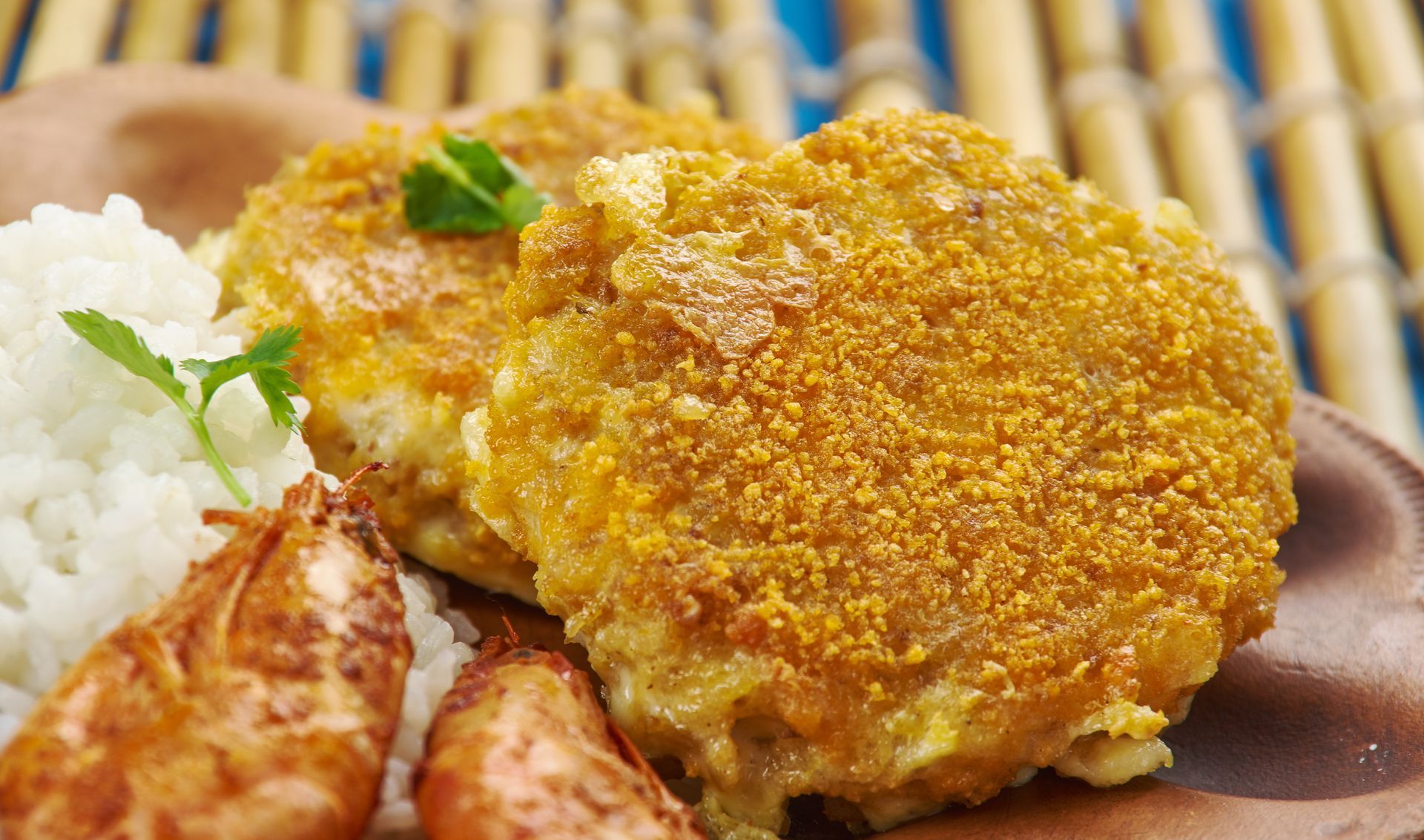 Two golden-brown patties, rice, and fried food on a brown plate, likely a meal.