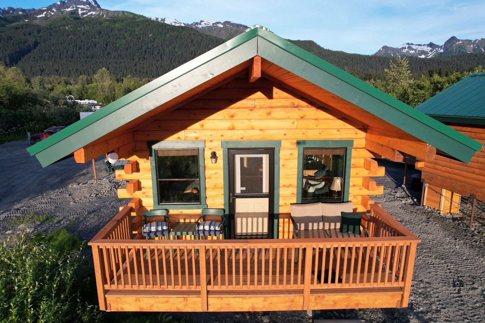 Wooden cabin with a green roof and porch. Mountains in the background.