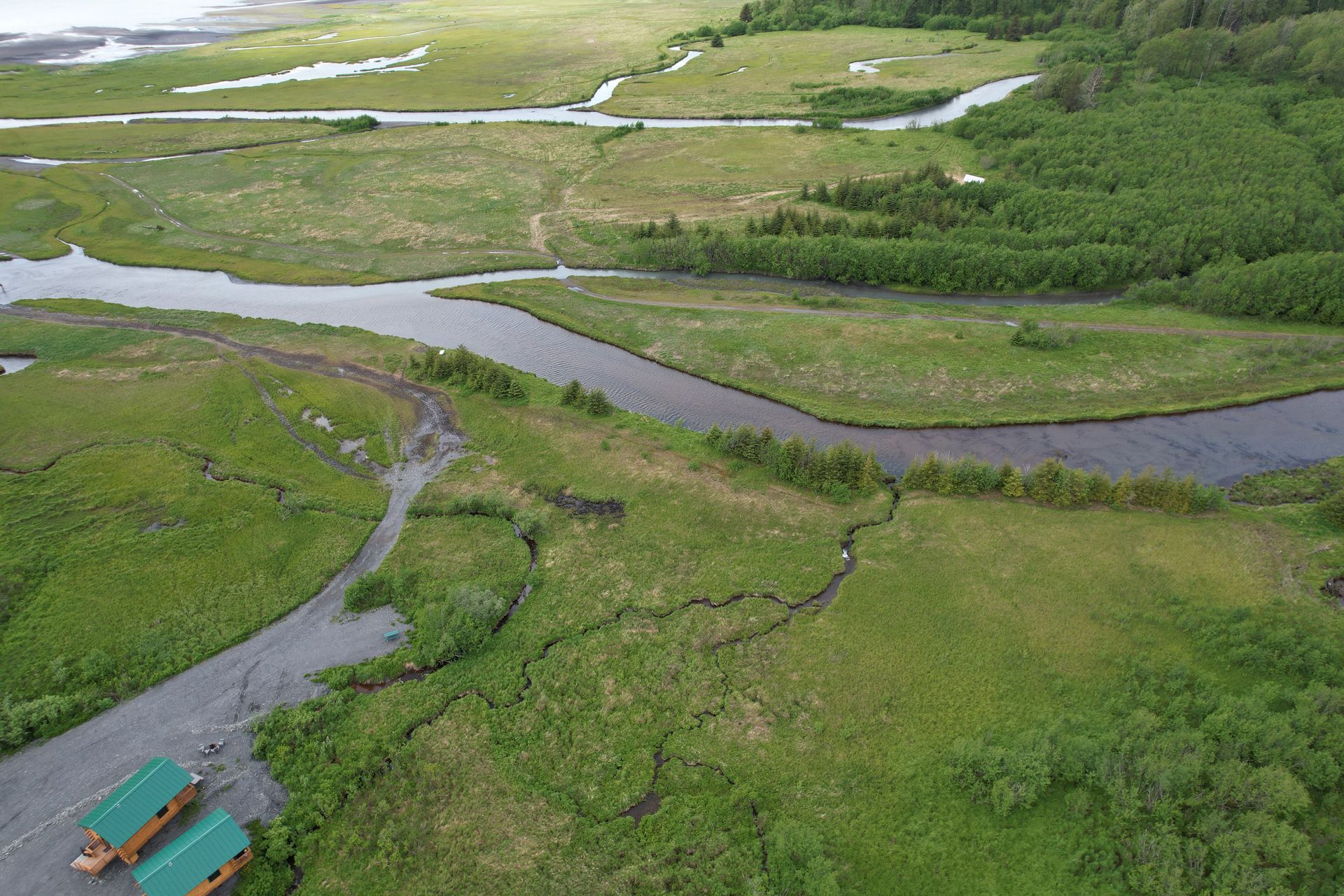 Overhead view of a river flowing through a lush green landscape. Two small cabins are visible at the bottom.