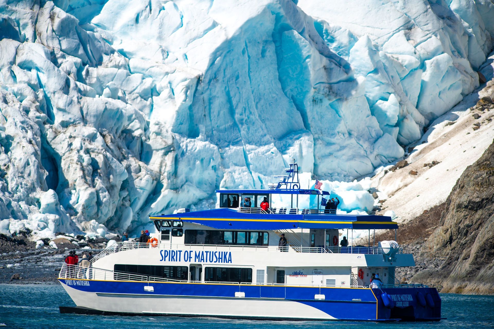 A large yacht is floating in the water near a glacier