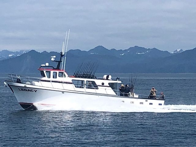 Boat on water in front of mountains. Partially cloudy sky.