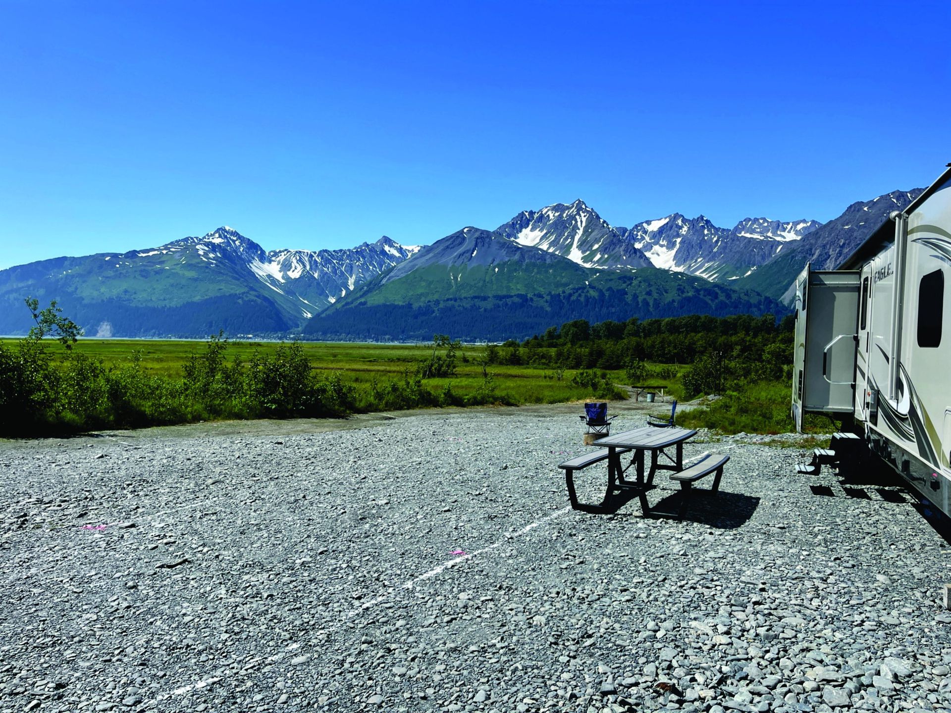 A rv is parked in a gravel lot with mountains in the background.