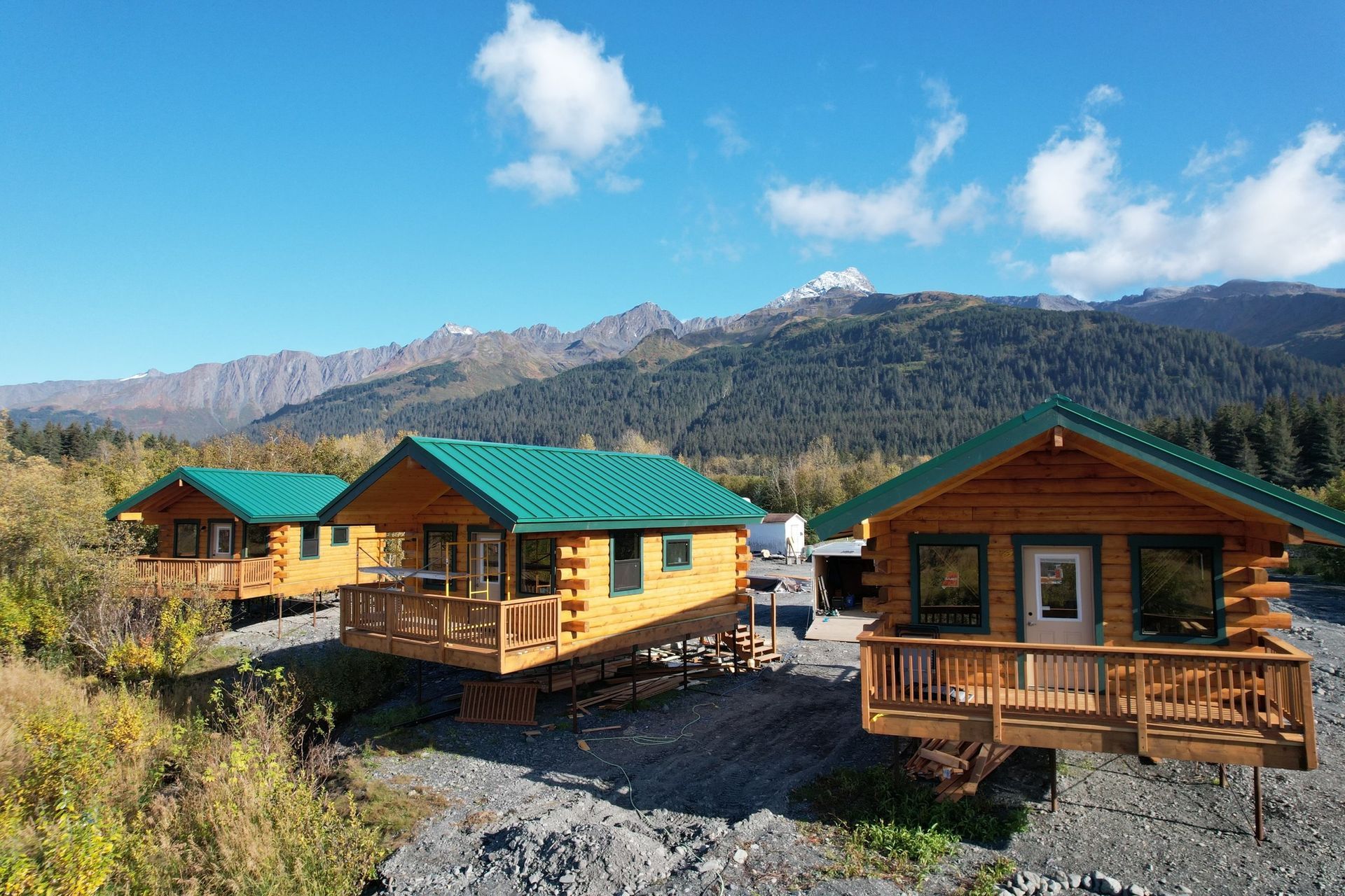 Two log cabins with green roofs and mountains in the background
