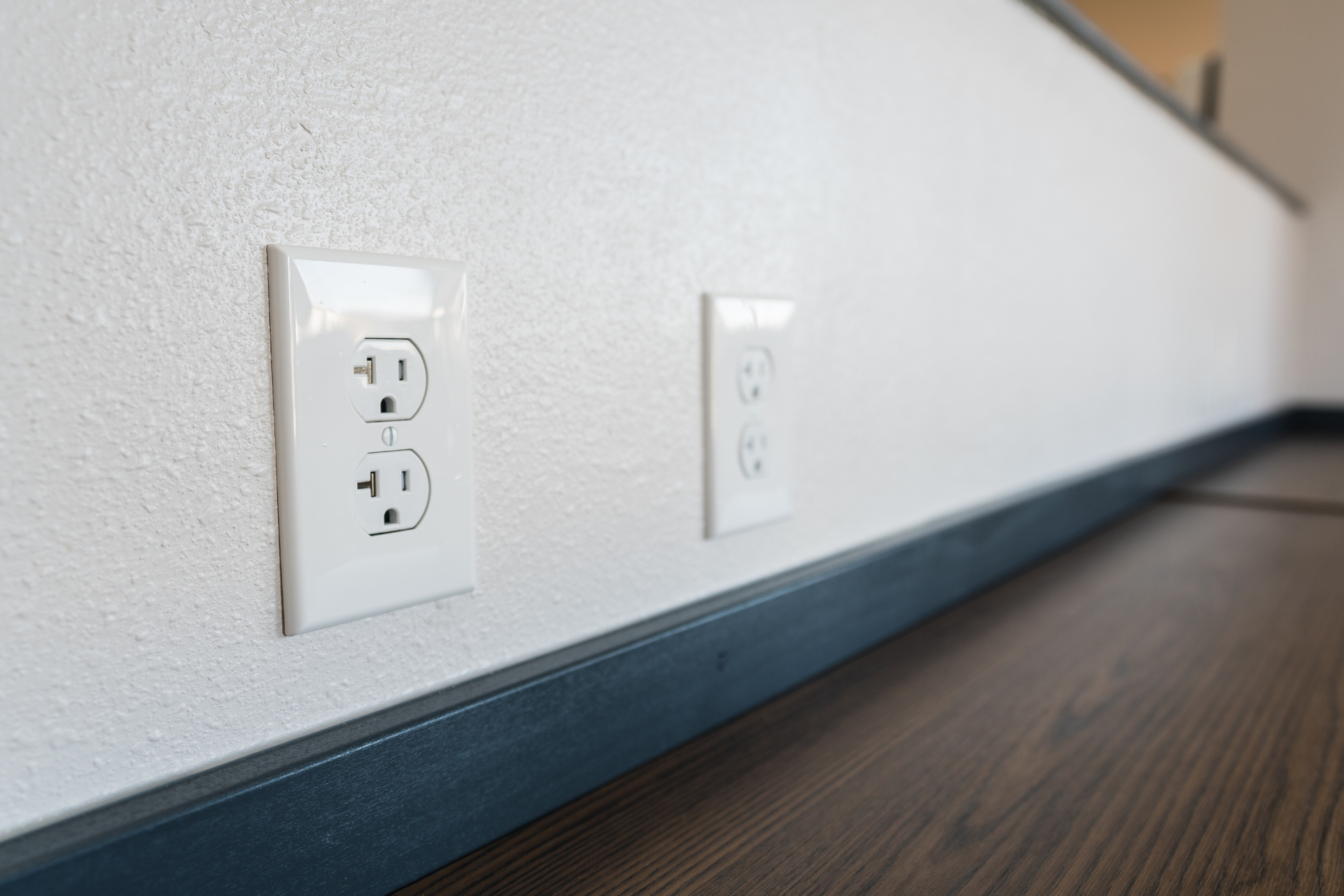 A couple of electrical outlets on a wall next to a wooden floor.