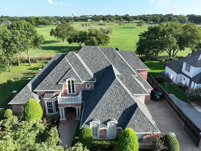 An aerial view of a large brick house with a gray roof surrounded by trees.