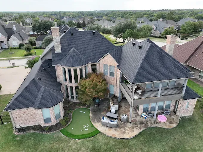 An aerial view of a large house with a putting green in the backyard.