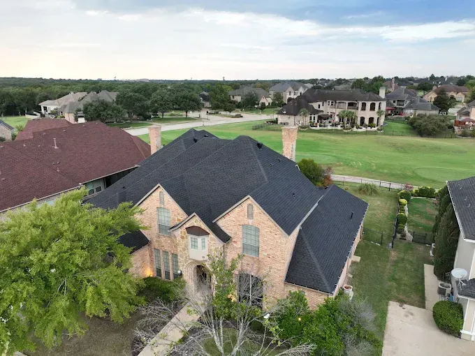 An aerial view of a large brick house with a black roof in a residential area.