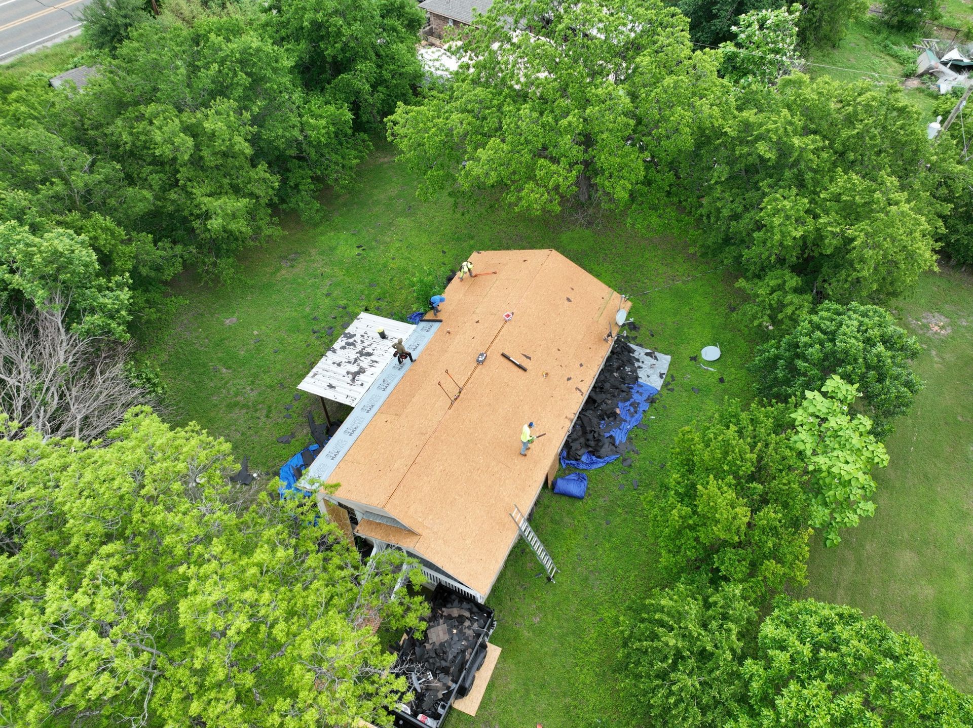 An aerial view of a house with a roof being installed surrounded by trees.