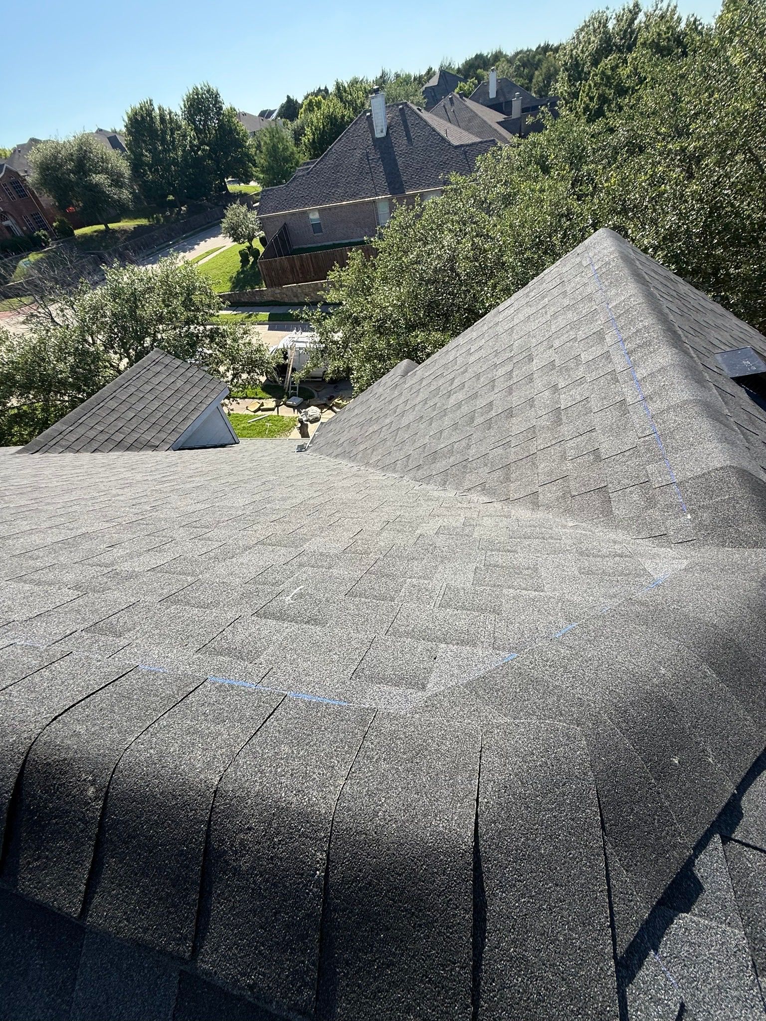 A roof with a lot of shingles on it is surrounded by trees and houses.