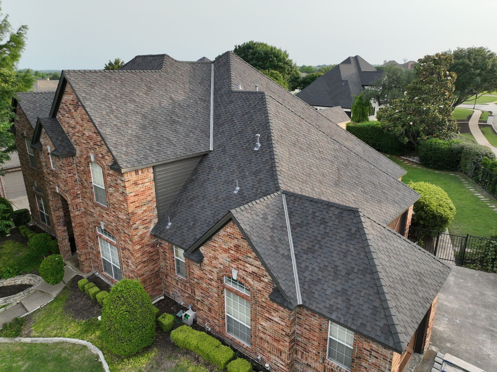 An aerial view of a large brick house with a black roof.