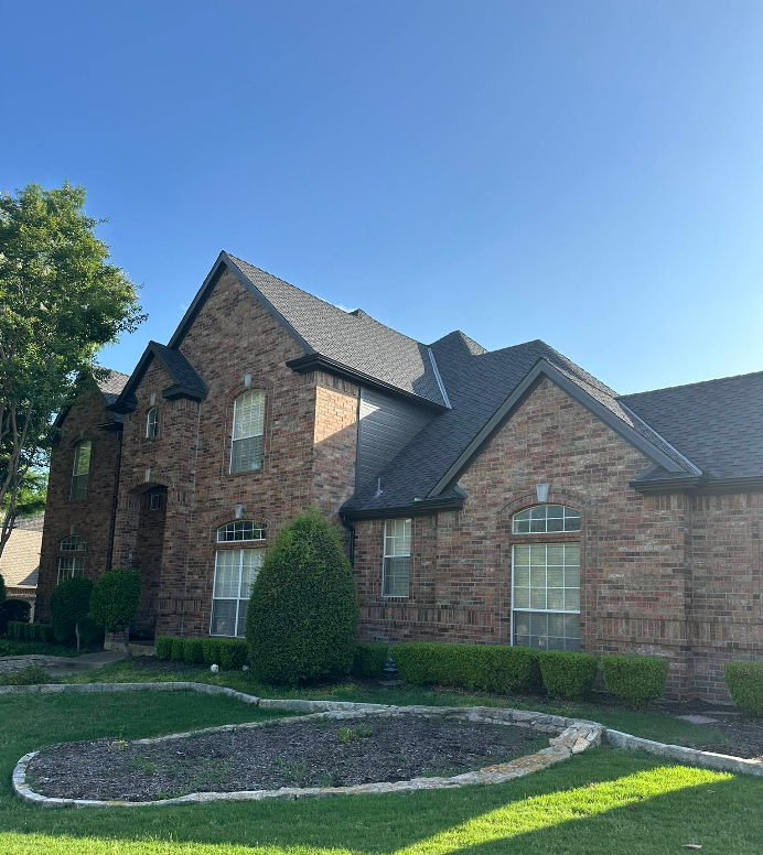 A large brick house with a black roof is sitting on top of a lush green lawn.