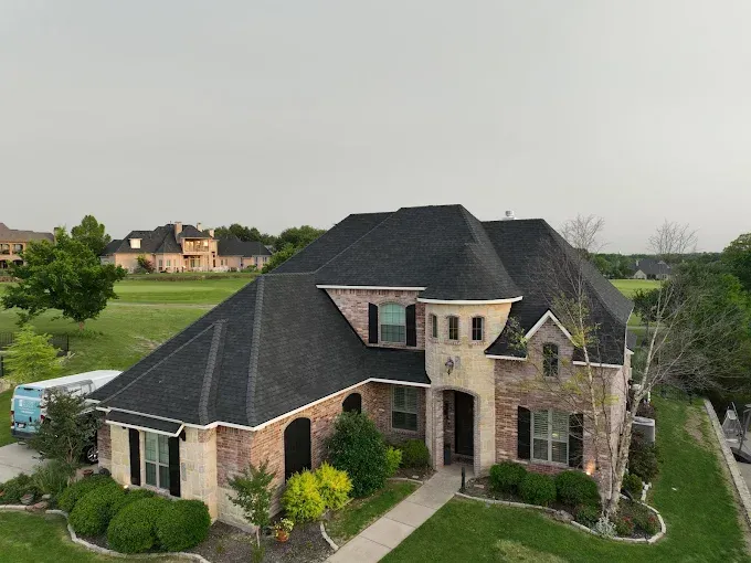 An aerial view of a large brick house with a black roof