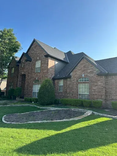 A large brick house with a black roof is sitting on top of a lush green lawn.