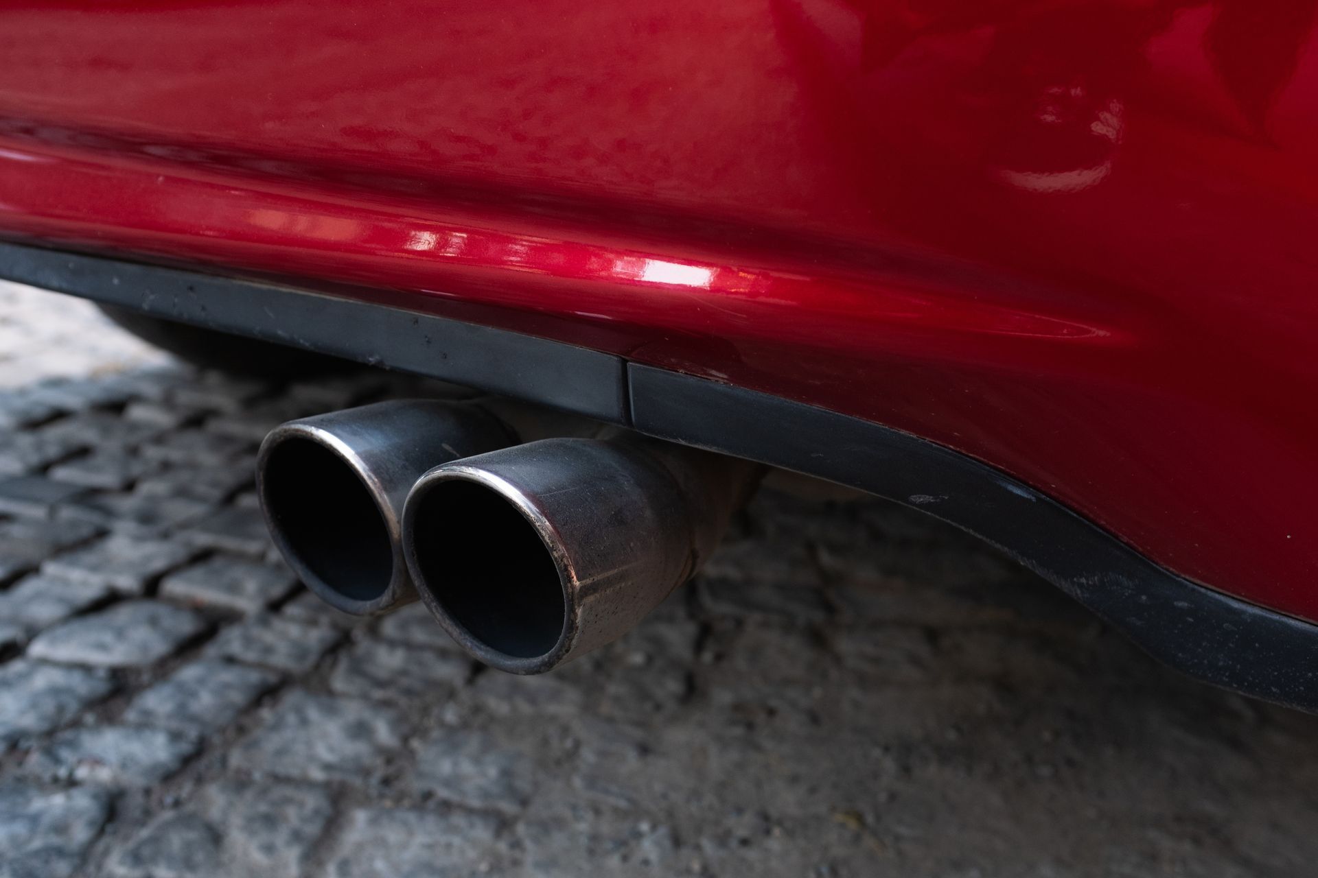 A red car with two exhaust pipes is parked on a cobblestone street.