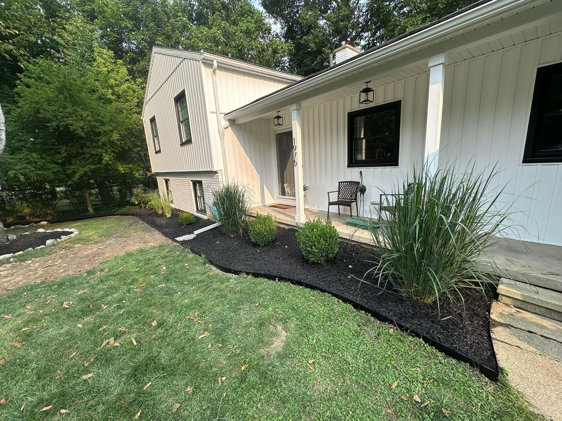 Front landscape bed renovation with metal edging, fresh mulch, new shrubs, and ornamental grasses at a home in Okemos, Michigan
