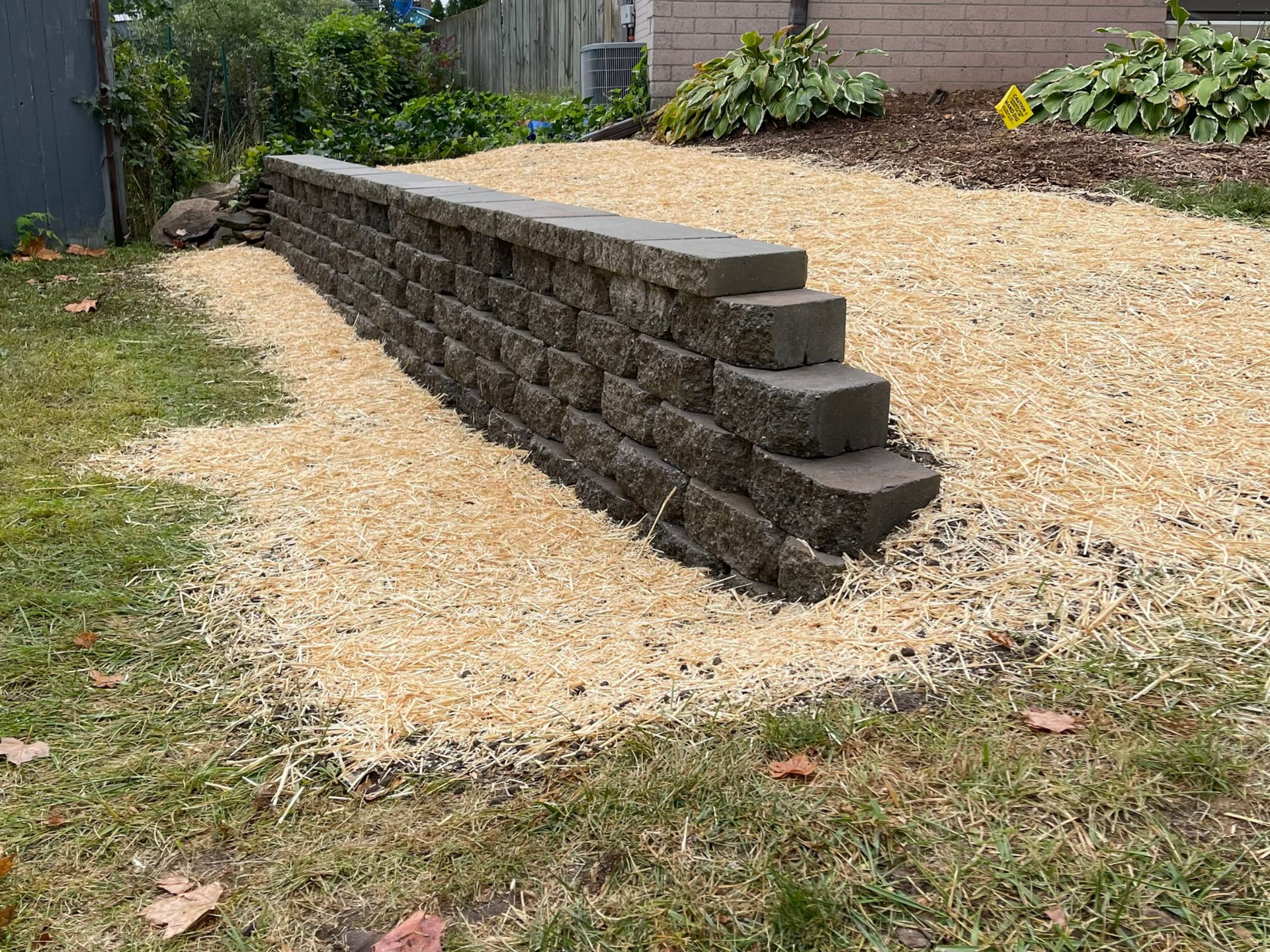 Retaining wall installation with grading and straw erosion control in Lansing, Michigan.