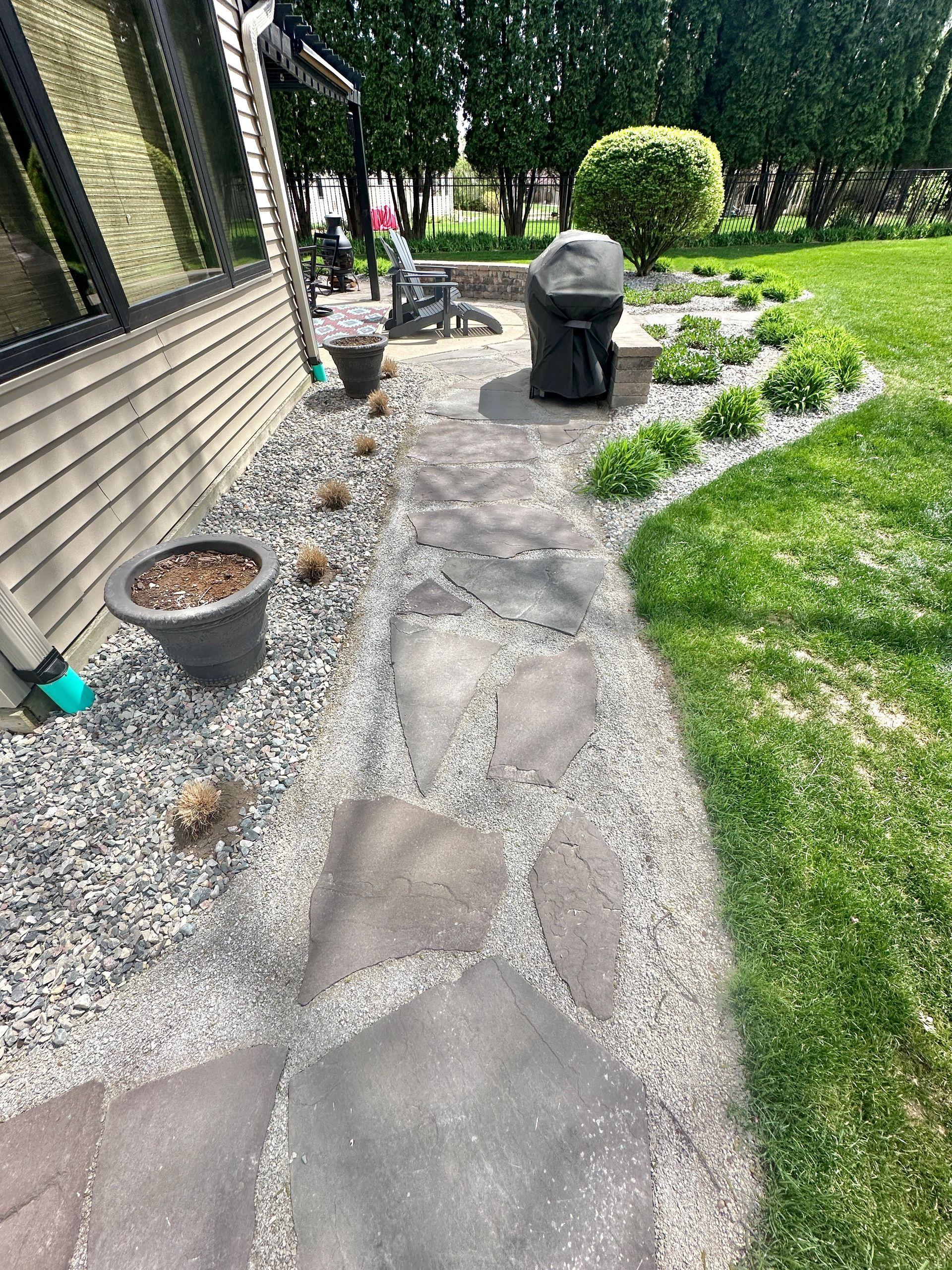 Flagstone walkway installation with decorative crushed stone landscape beds and curved lawn edge in East Lansing, Michigan