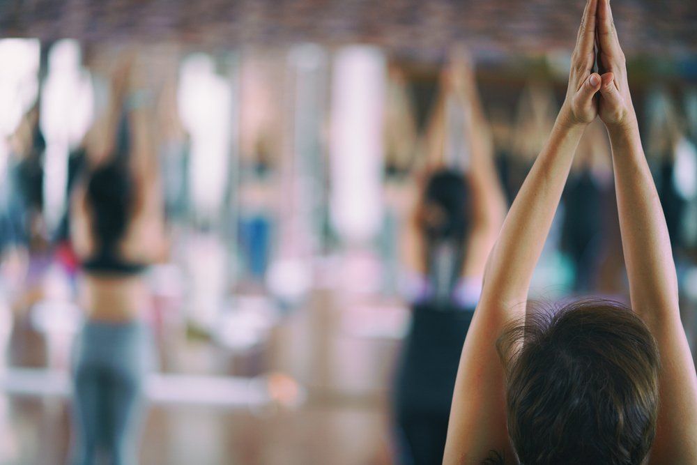 People meditating in a brightly lit room, hands in Gyan mudra, seated cross-legged on the floor.