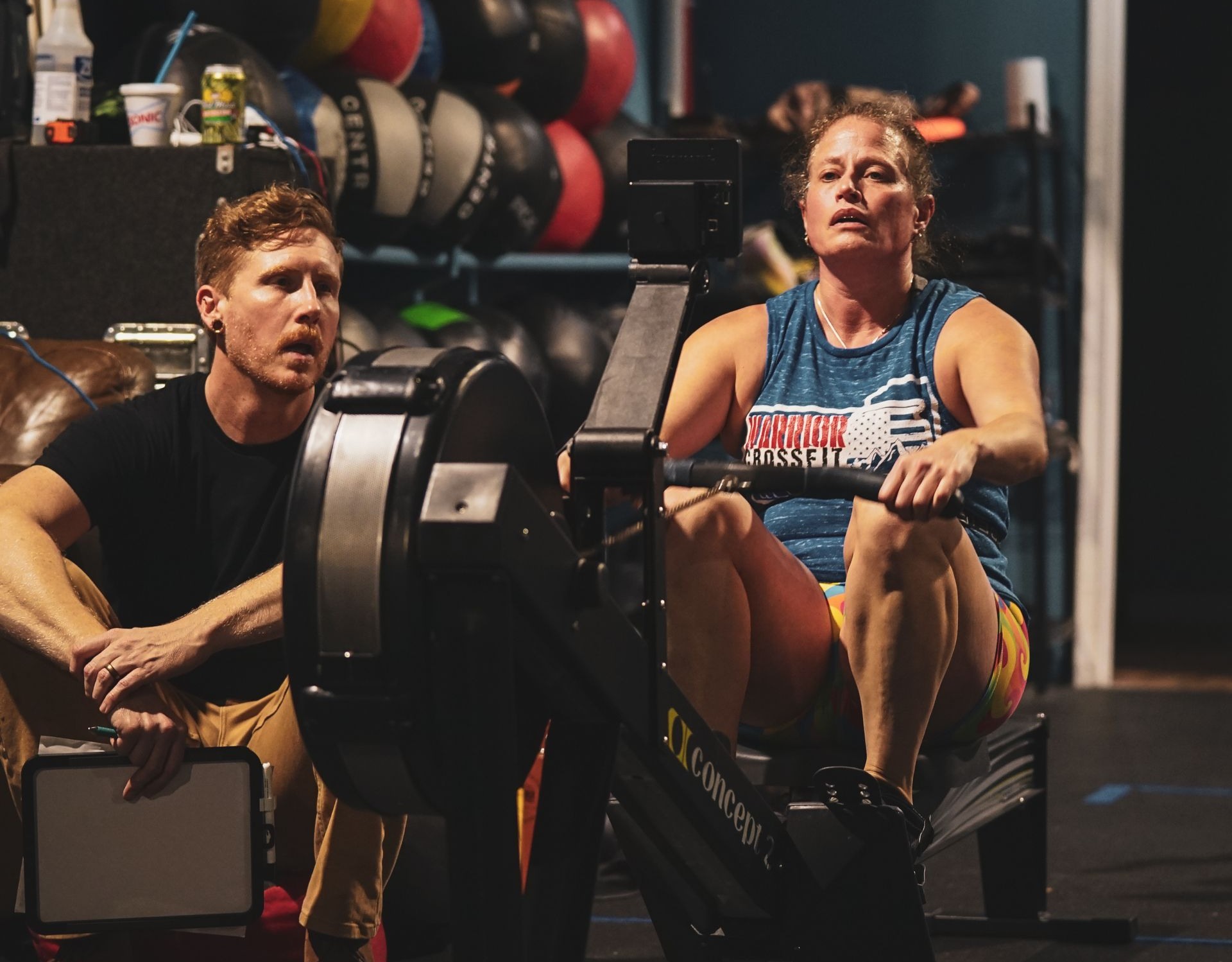 Woman doing dumbbell chest press with assistance from trainer at a gym.