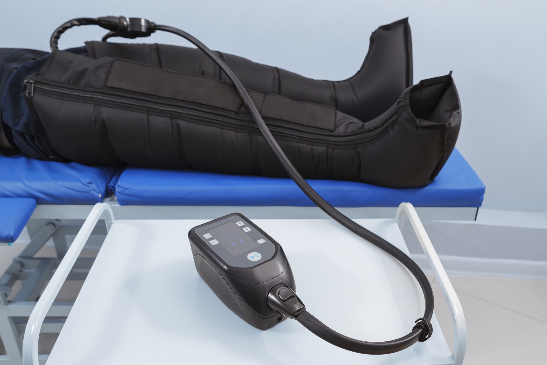Person using pneumatic compression therapy on legs with control unit on a table.