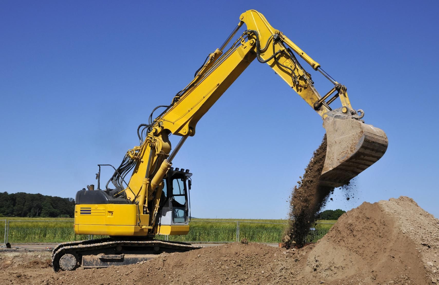 Un escavatore giallo sta scavando un mucchio di terra