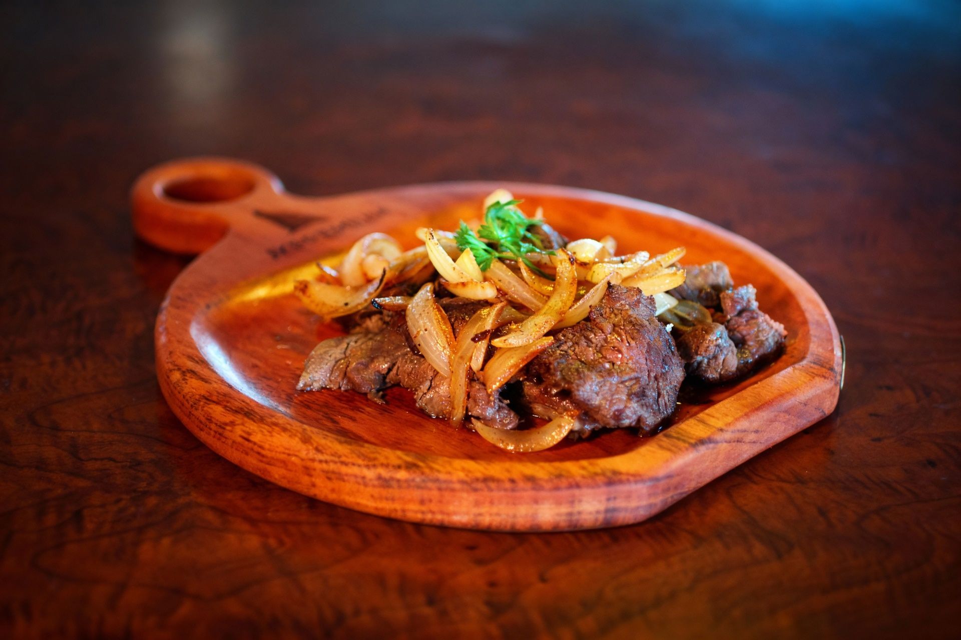 Bife com cebolas salteadas e ervas aromáticas servido em uma tábua de madeira.
