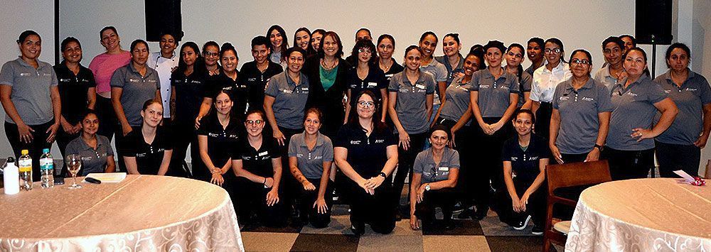Foto de grupo de um grande grupo de mulheres e alguns homens posando ao redor de duas mesas redondas.